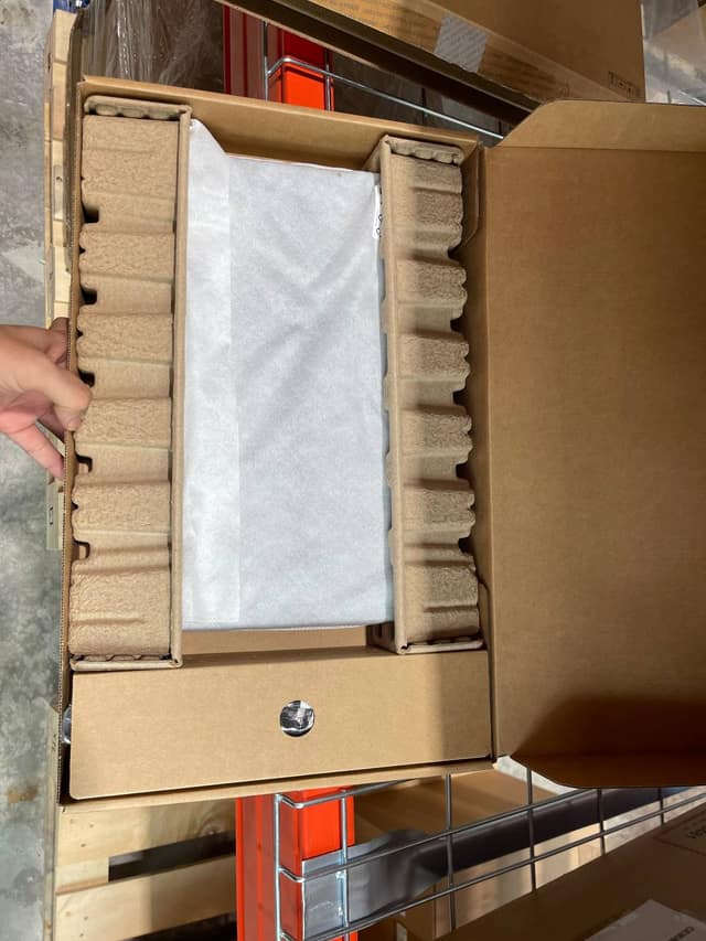 An Acer laptop in its open box on our shelf, in a white sleeve between two card holders